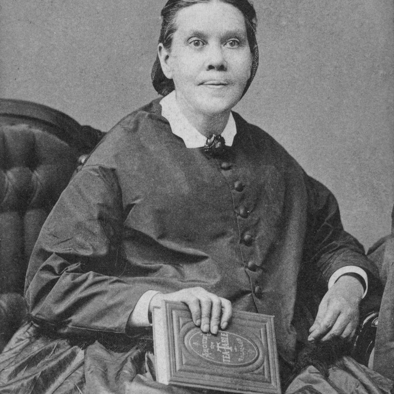 Ellen G. White seated, holding a bound book, photographed in 1878