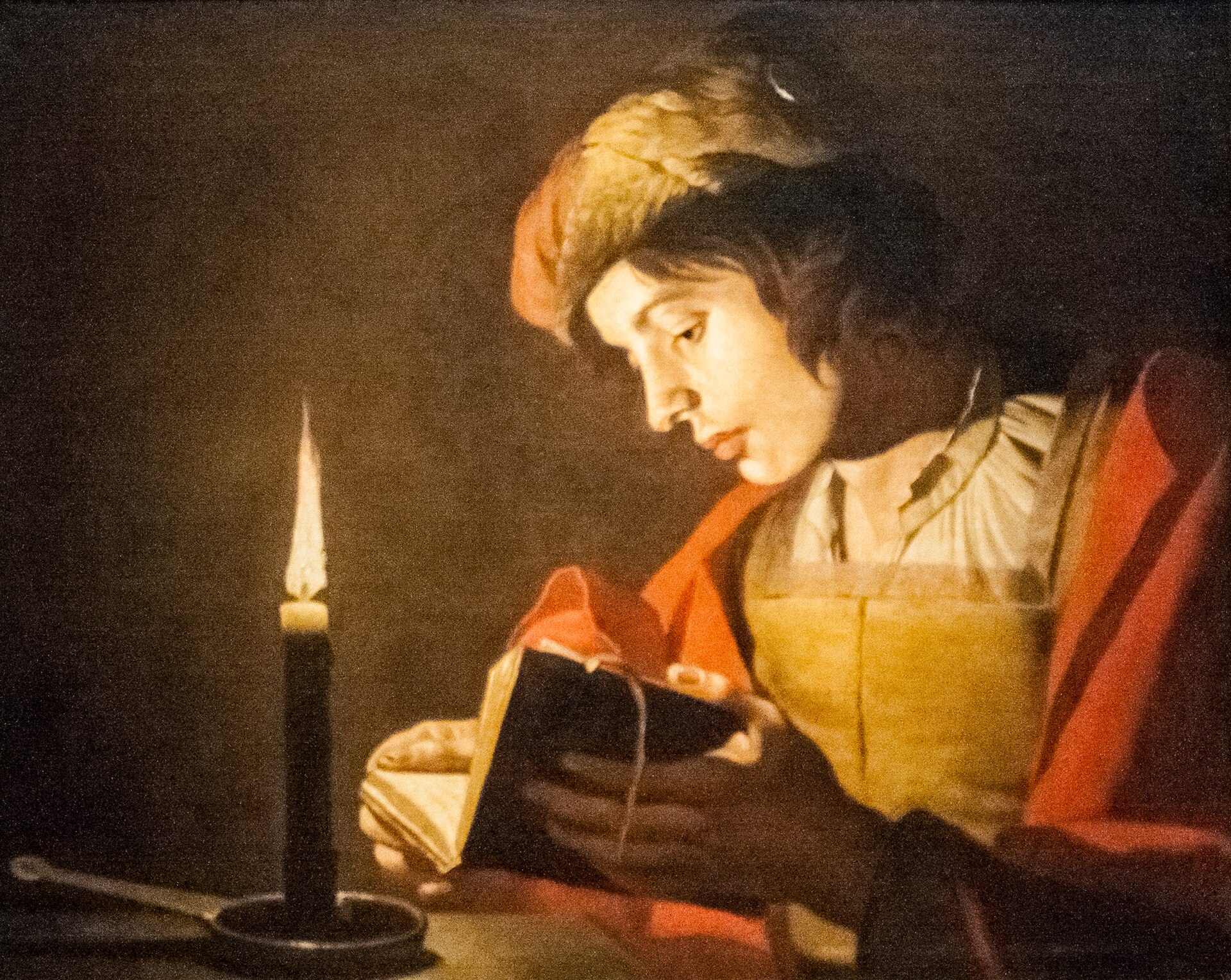 Stom's painting of a young man in a red cloak reading a small book intently by the light of a single candle