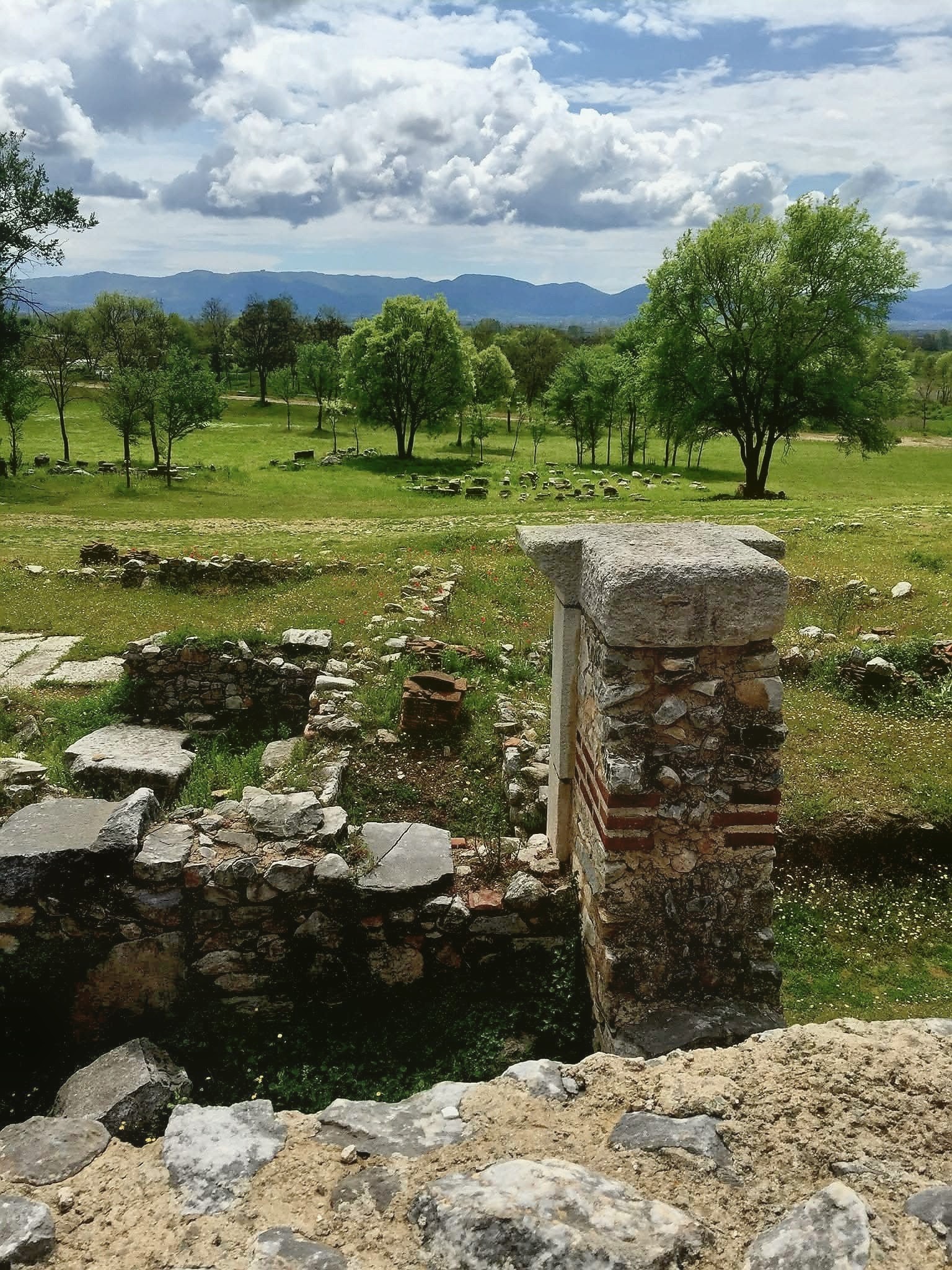 For To Me To Live Is Christ 1 Stone walls and a brick-banded pier among the grassy ruins of ancient Philippi, with trees and the mountains of Macedonia beyond