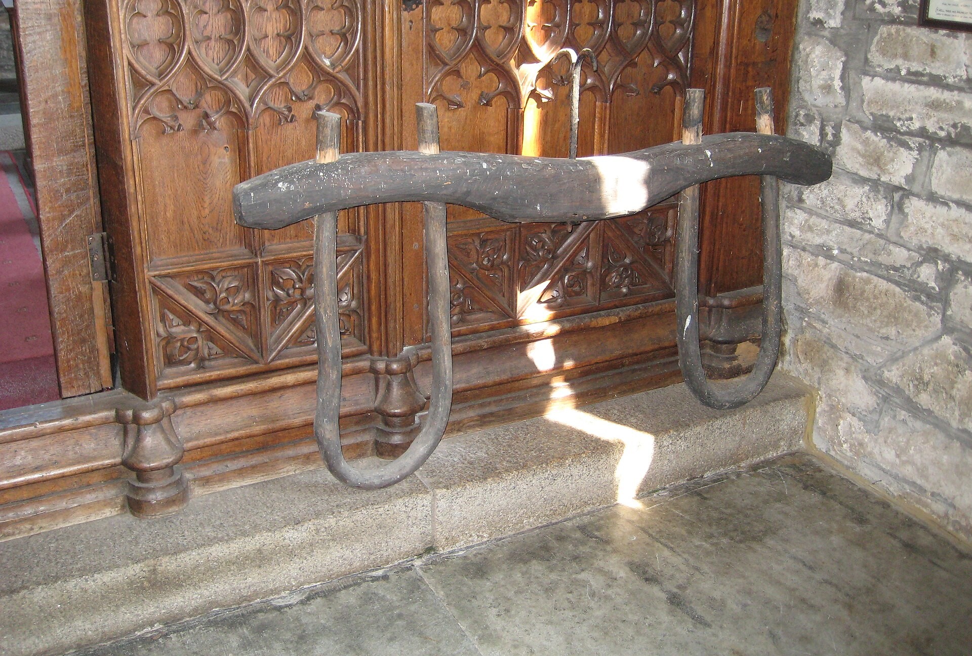 The Yoke And The False Prophet 1 A heavy old wooden ox yoke with two curved iron bows, resting against a carved wooden screen inside a stone church